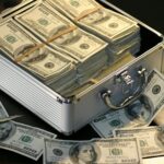 Stacks of $100 bills bound with bands inside a metal briefcase, money overflowing around it