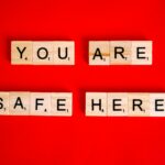 Scrabble tiles spell 'YOU ARE SAFE HERE' on a red surface, conveying a reassuring message.