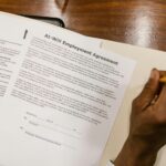 Hand signing an At-Will Employment Agreement on a wooden desk.