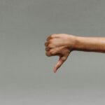 Arm extended to the right with a hand showing a thumbs-down gesture against a gray background, conveying disapproval